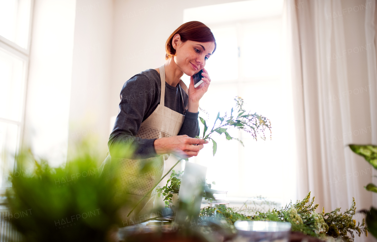 A young creative woman arranging flowers in a flower shop, using smartphone. A startup of florist business.