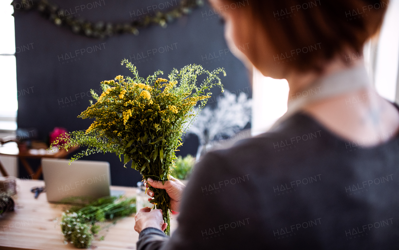 A midsection of young creative woman arranging flowers in a flower shop. A startup of florist business. Rear view.