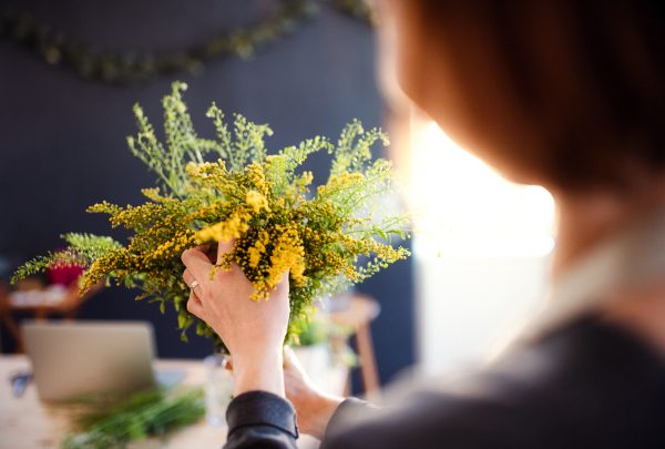 A midsection of young creative woman arranging flowers in a flower shop. A startup of florist business. Rear view.