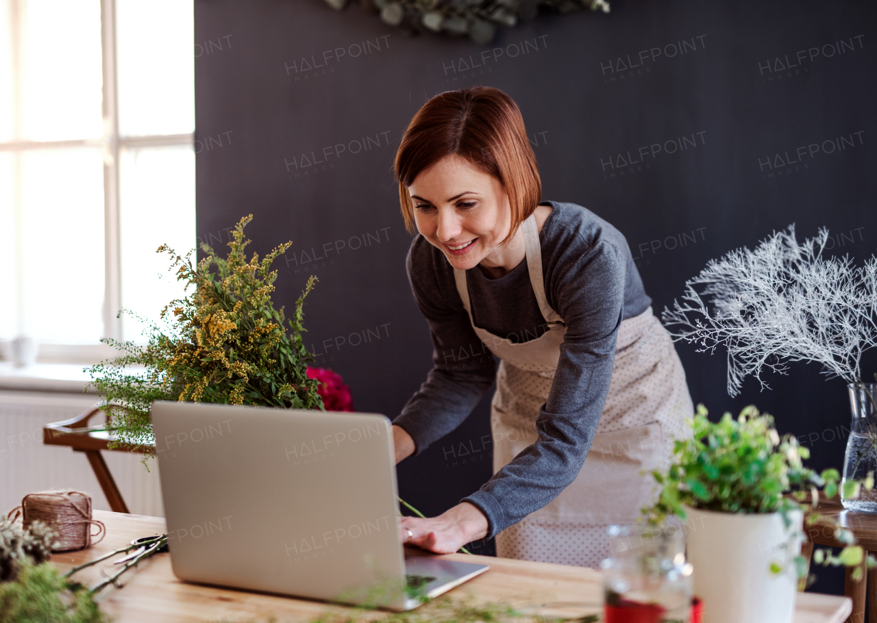 A young creative woman arranging flowers in a flower shop, using laptop. A startup of florist business.