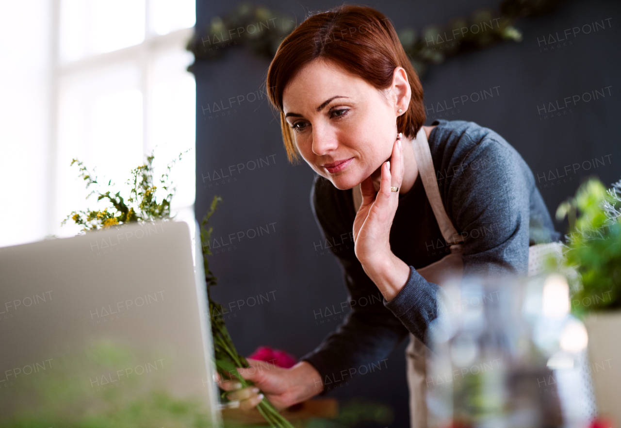 A young creative woman arranging flowers in a flower shop, using laptop. A startup of florist business.