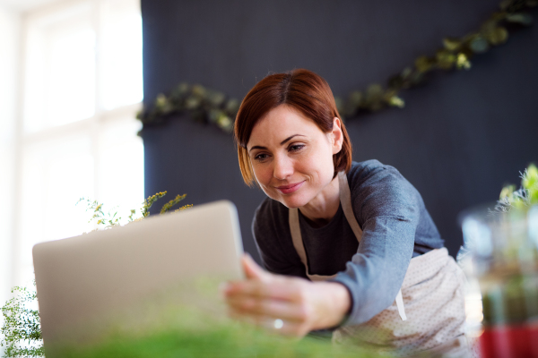 A young creative woman arranging flowers in a flower shop, using laptop. A startup of florist business.