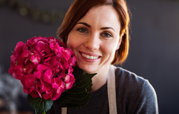 A portrait of young creative woman arranging flowers in a flower shop. A startup of florist business.