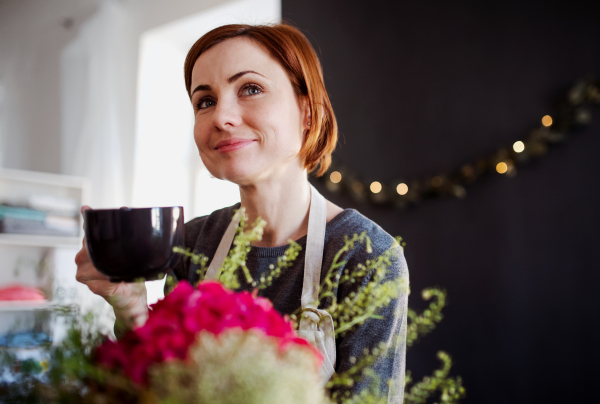 A young creative woman with a coffee arranging flowers in a flower shop. A startup of florist business.