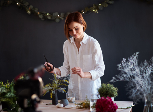 A young creative woman blogger or vlogger arranging flowers in a flower shop. A startup of florist business.