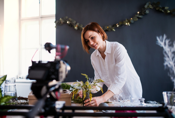 A young creative woman blogger or vlogger arranging flowers in a flower shop. A startup of florist business.