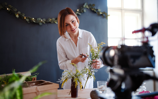 A young creative woman blogger or vlogger arranging flowers in a flower shop. A startup of florist business.