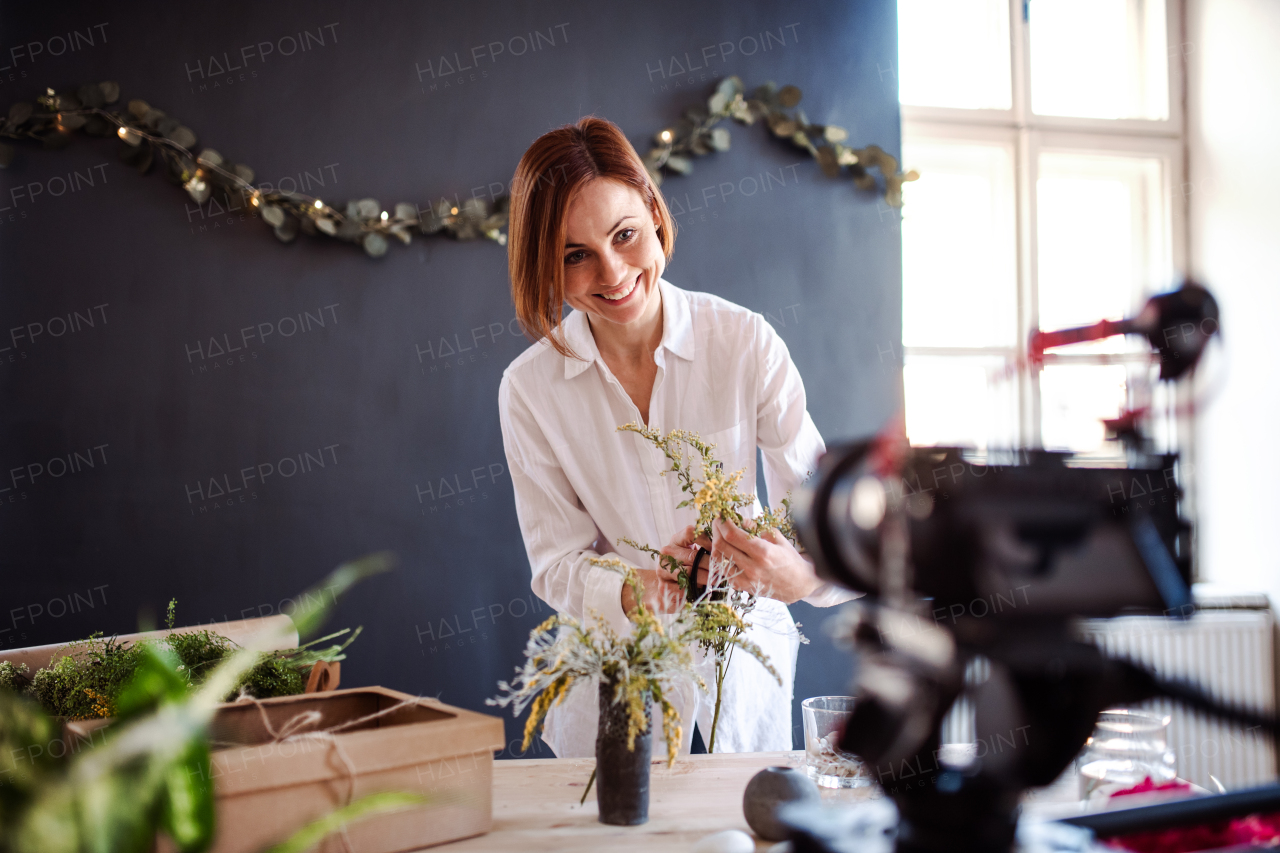 A young creative woman blogger or vlogger arranging flowers in a flower shop. A startup of florist business.