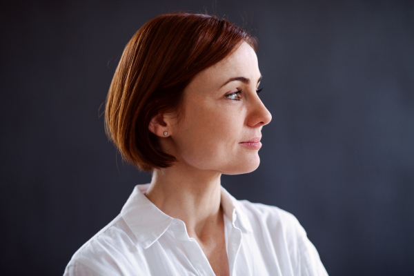 A close-up portrait of young beautiful woman standing against dark background.