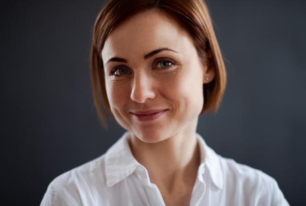 A close-up portrait of young beautiful woman standing against dark background.