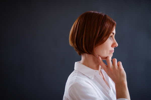 A side view portrait of young beautiful woman standing against dark background.