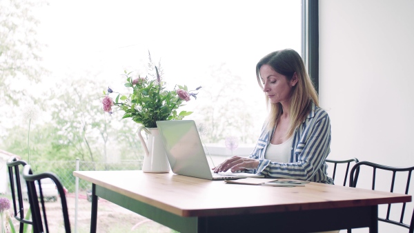 A confident mature woman sitting at the table, working with laptop in home office.