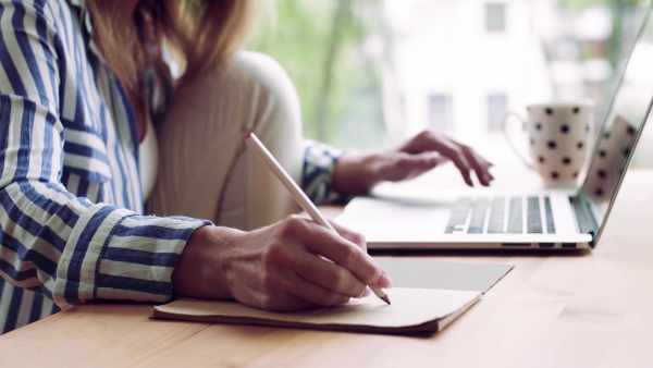 A confident mature woman sitting at the table, working with laptop in home office.