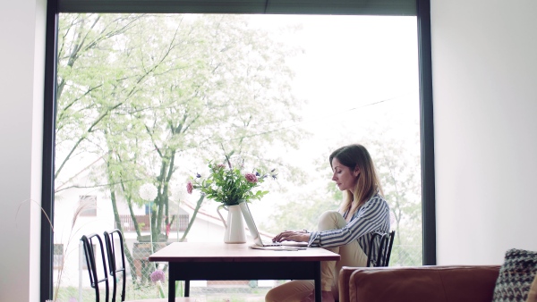 A confident mature woman sitting at the table, working with laptop in home office.