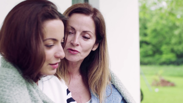 A close-up of mother with adult daughter sitting at the table outdoors, drinking coffee.