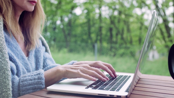 A midsection of mature woman sitting at the table on a terrace outdoors, working with laptop.