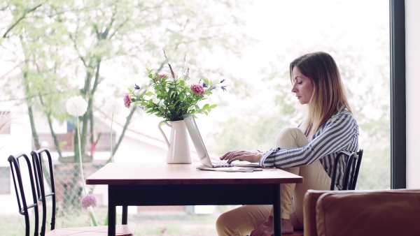 A confident mature woman sitting at the table, working with laptop in home office.