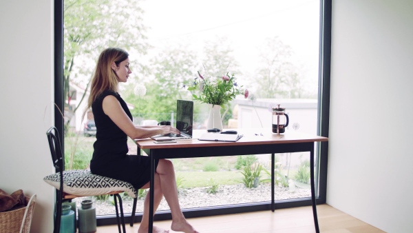 A confident mature woman sitting at the table, working with laptop in home office.