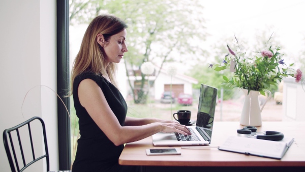 A confident mature woman sitting at the table, working with laptop in home office.