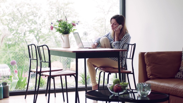 A confident mature woman sitting at the table, working with laptop in home office.