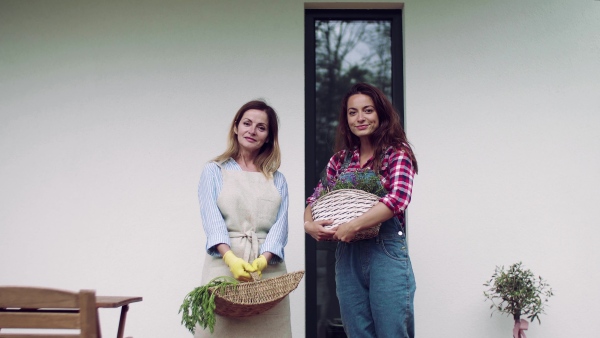 A front view portrait of mother with adult daughter on terrace outdoors, gardening.