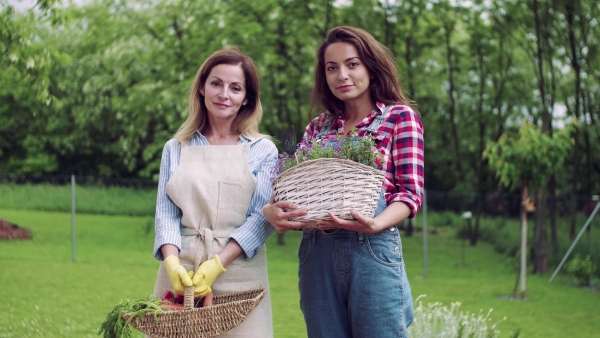 A portrait of mother with adult daughter standing in garden outdoors, gardening.