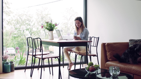 A mature woman with laptop and smartphone sitting at the table, working in home office.