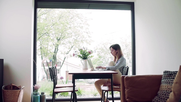 A mature woman with coffee and laptop indoors working in home office. Slow motion.