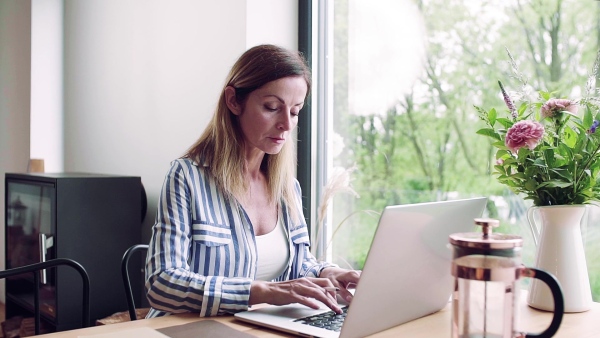 A confident mature woman sitting at the table, working with laptop in home office. Slow motion.