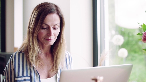 A confident mature woman sitting at the table, working with laptop in home office. Slow motion.