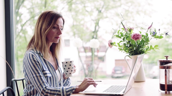 A confident mature woman sitting at the table, working with laptop in home office. Slow motion.