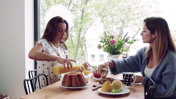 A happy mother with adult daughter sitting at the table indoors, having breakfast. Slow motion.