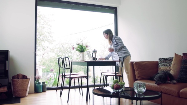 A mature woman with coffee and laptop indoors working in home office.