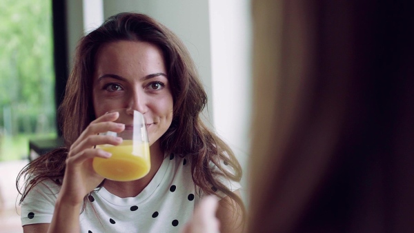 Young woman with unrecognizable mother sitting at the table indoors, drinking juice. Slow motion.