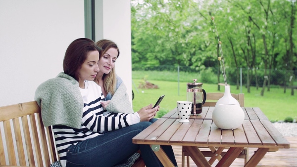 A mother with adult daughter sitting at the table outdoors on a terrace, using smartphone. Slow motion.