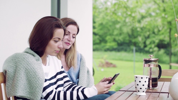 A mother with adult daughter sitting at the table outdoors on a terrace, using smartphone. Slow motion.