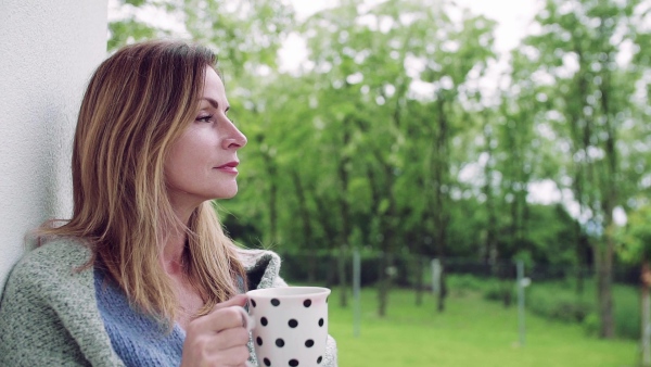 A mature woman with tea and blanket standing outdoors on terrace. Slow motion.