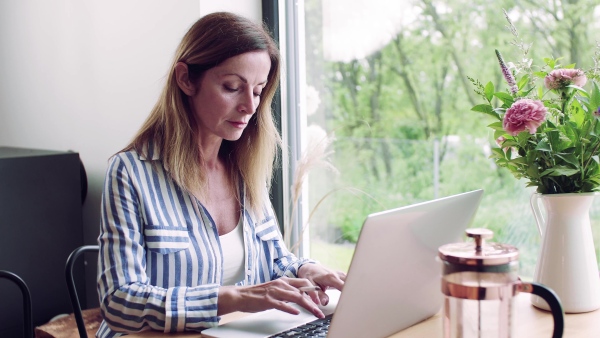 A confident mature woman sitting at the table, working with laptop in home office.