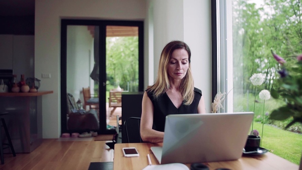 A confident mature woman sitting at the table, working with laptop in home office. Slow motion.