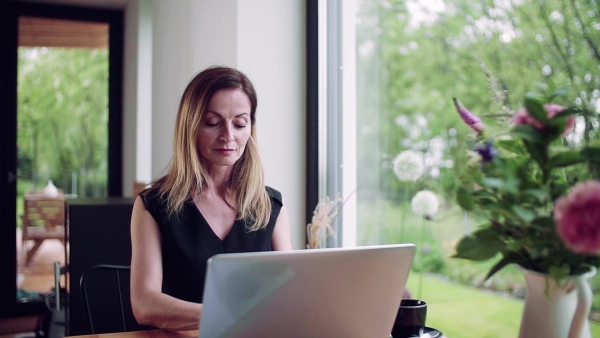 A confident mature woman sitting at the table, working with laptop in home office. Slow motion.