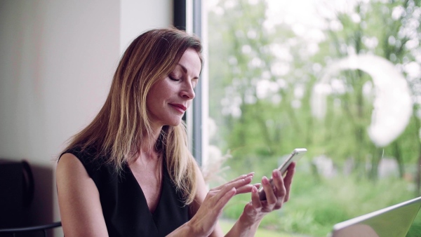 Mature woman sitting at the table in home office, using smartphone. Slow motion.