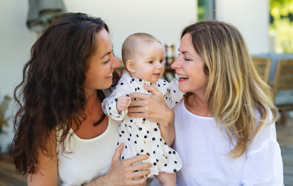 Woman with daughter and baby granddaughter resting outdoors in backyard, bonding.