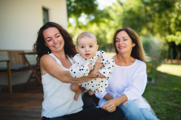 Woman with daughter and baby granddaughter resting outdoors in backyard, bonding.