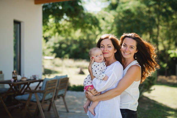 Woman with daughter and baby granddaughter resting outdoors in backyard, bonding.