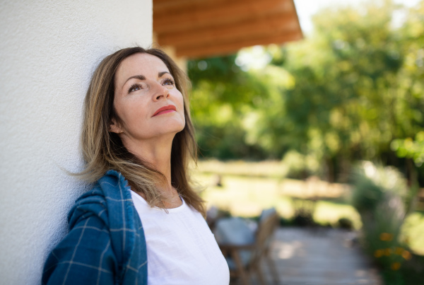 Portrait of mature woman resting outdoors, leaning on wall of house.