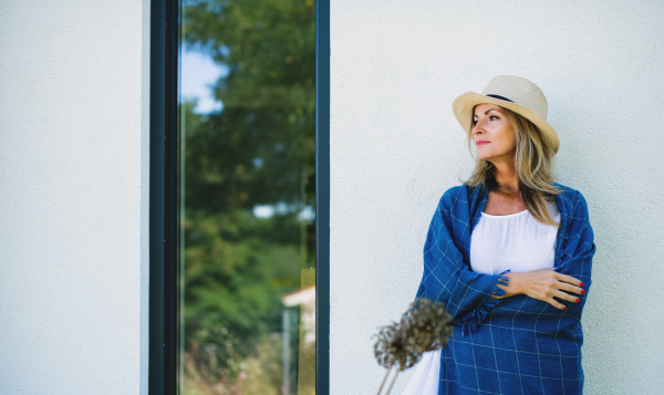 Portrait of mature woman resting outdoors, leaning on wall of house.