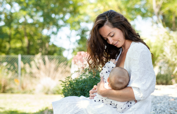 Portrait of woman nursing baby girl outdoors in backyard.