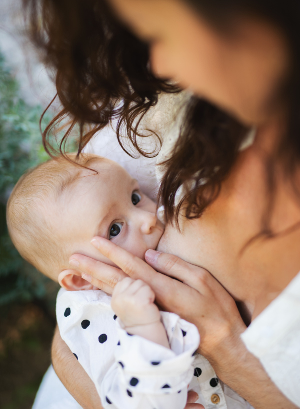 Top view of unrecognizable woman nursing baby girl outdoors in backyard.