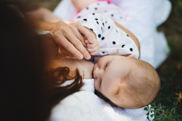 Top view of unrecognizable woman nursing baby girl outdoors in backyard.