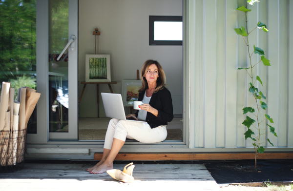 Front view of mature woman working in home office in container house in backyard.